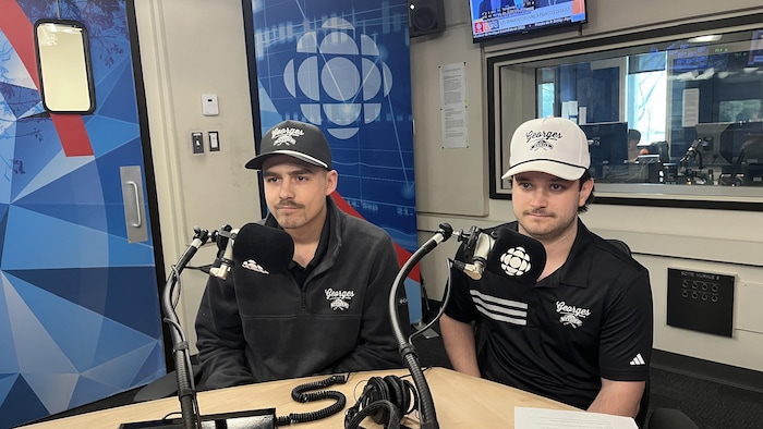 Deux personnes sont à l'arrière de deux micros dans un studio radio.