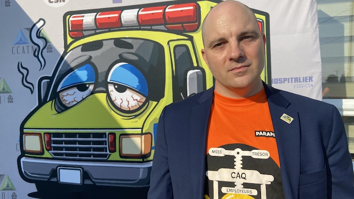 Félix-Antoine Lafleur debout pour se faire prendre en photo, devant une l'affiche où on voir le dessin d'une ambulance