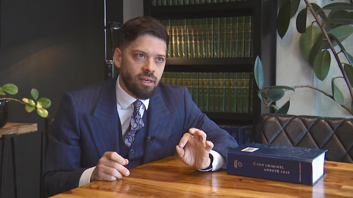 L'homme vêtu d'un complet bleu assis à une table devant une bibliothèque.