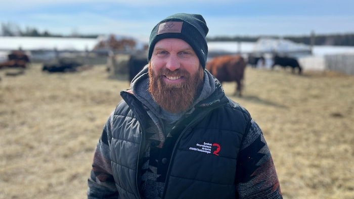 Dans un champ avec des vaches, Félix Désaulniers porte un manteau du Syndicat des producteurs de bovins de l'Abitibi-Témiscamingue.
