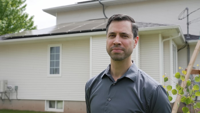 Un homme devant sa maison aux toits couverts de panneaux solaires.