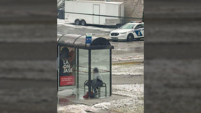Une femme dans un abribus et une voiture de police plus loin. 