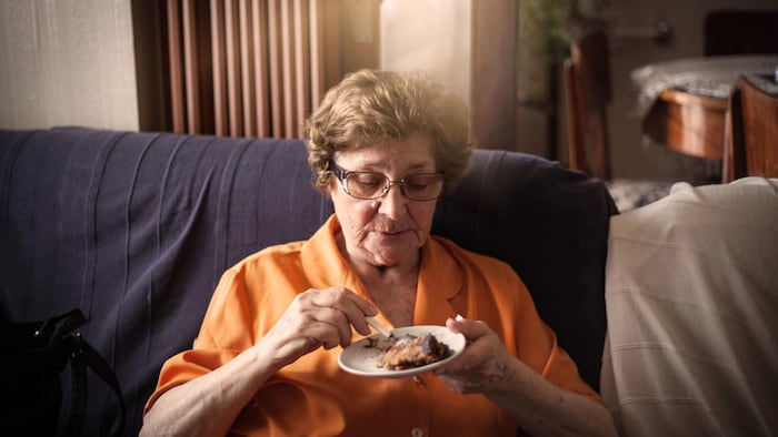 Une dame mange un morceau de tarte au chocolat dans son salon.