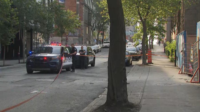 Des policiers bloquent une partie de la rue où un ruban a été mis pour délimiter la scène.