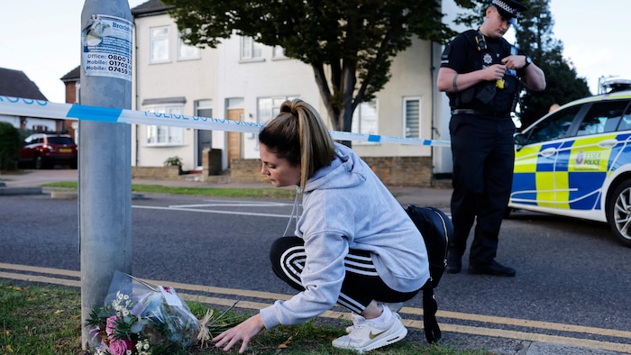 Une jeune femme dépose un bouquet de fleurs au pied d'un lampadaire.