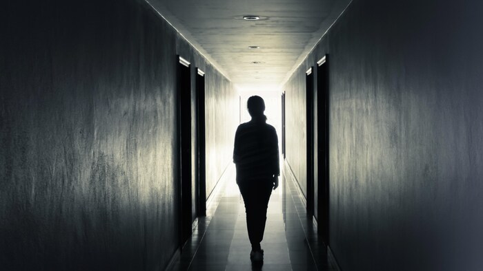 Une femme, vue de dos, marche seule dans un corridor étroit.