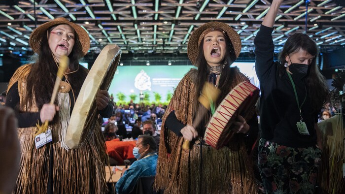 امرأتان من السكان الأصليين تقرعان الطبول وتغنيان فيما تقوم امرأة ثالثة بالرقص.