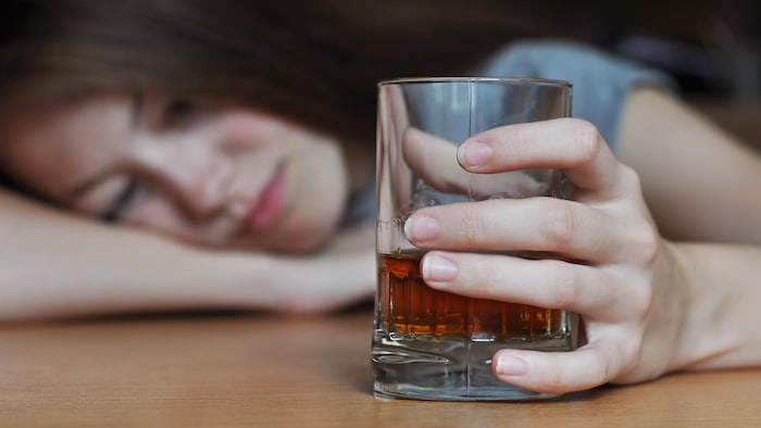 Une femme tient un verre d'alcool à la main, la tête posée sur la table.