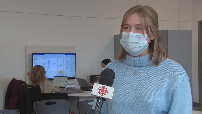Une jeune femme en entrevue avec une journaliste. Elle porte un masque. Un micro est posé devant elle.