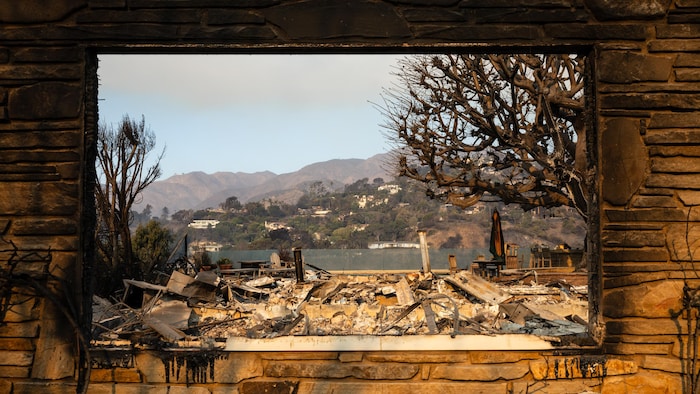 Le reste d'une fenêtre sans vitre donne sur le quartier de Pacific Palisades, ravagé par les feux.