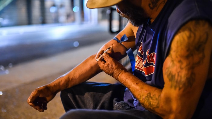 Un homme s'injecte de l'héroïne dans la rue, la nuit.