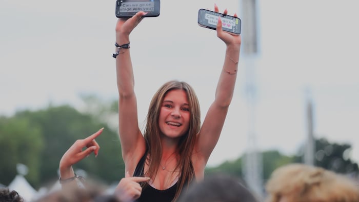 Une jeune fille tient des téléphones, avec un message, dans la foule.