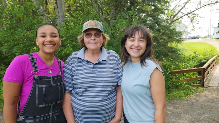 Trois femmes sourient pour la photo devant un îlot de verdure.