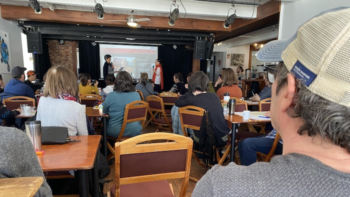 Environ 60 personnes assises dans un restaurant, face à une scène.