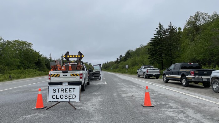 Des camions du gouvernement stationnés au bord de l'autoroute et une affiche indiquant que la route est fermée.
