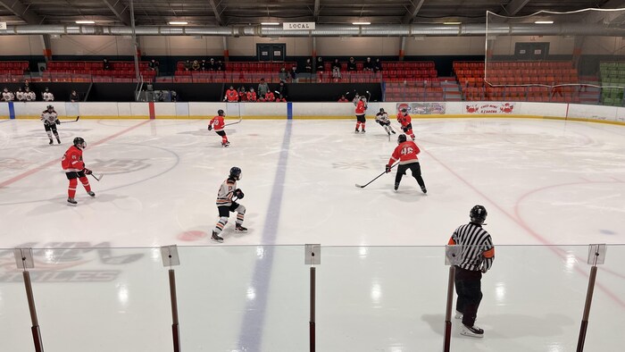 Des joueurs de Hockey s'affrontent sur la glace d'un aréna. Un arbitre rôde non loin.