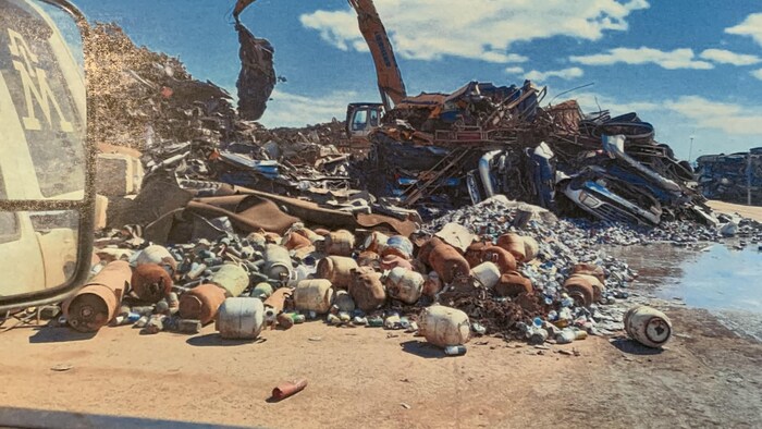 Une excavatrice, de la ferraille et des bonbonnes de propane entassées. 