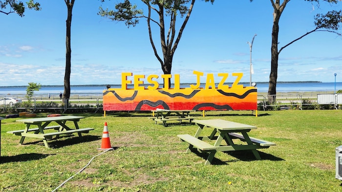 Une enseigne du Festi Jazz posée dans un parc, devant le fleuve.
