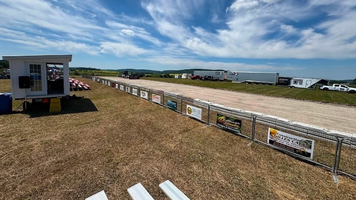 Une piste en terre battue bordée de clôtures avec des affiches de commanditaires.