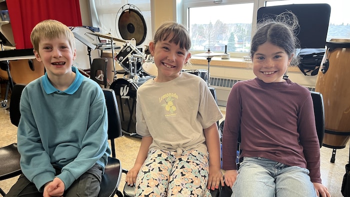 Les trois enfants sont assis côte à côte dans leur local de musique.