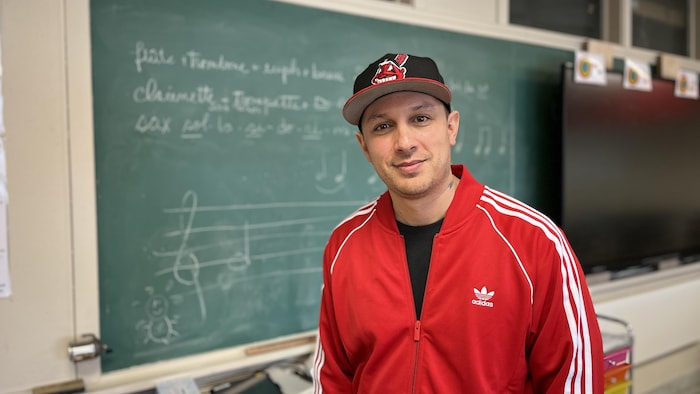 Samian pose devant le tableau dans le local de musique d'une école primaire.