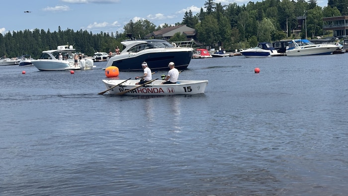 Deux personnes habillées en blanc dans une chaloupe sur un lac.
