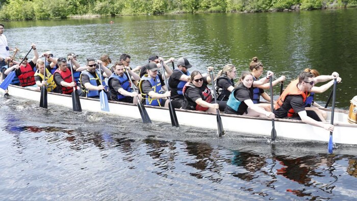 Un groupe de personnes rament à bord d'un long bateau sur une rivière.