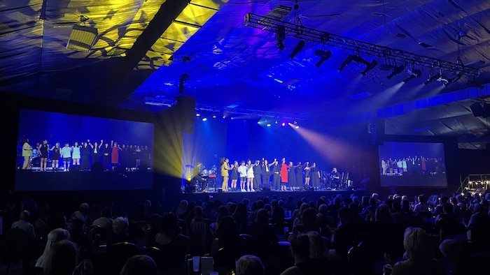 Un groupe de personnes sur une sc&egrave;ne salue une foule.