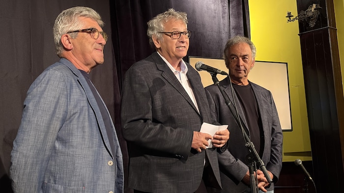 Louis Dallaire, Jacques Matte et Guy Parent, debout sur une petite scène, s'adressent aux gens.