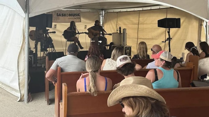 Des musiciens jouant de la guitare acoustique sur une scène couverte d'une tente.