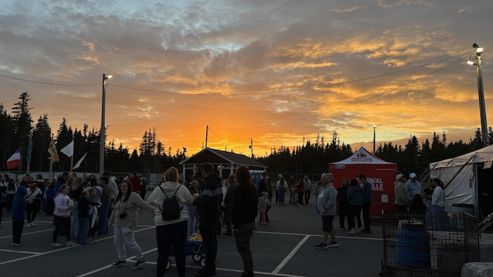 Les festivaliers se rassemblent sur le site extérieur alors que le ciel se pare d'un coucher de soleil derrière les tentes.