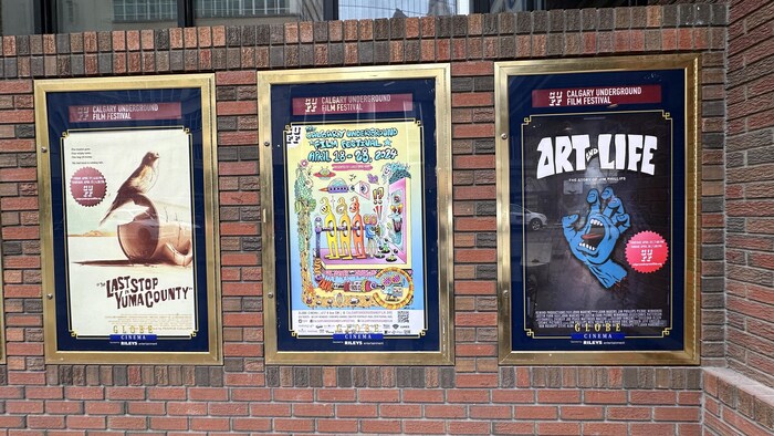 Trois affiches de films présentés dans le cadre du festival sont sur un mur de brique.