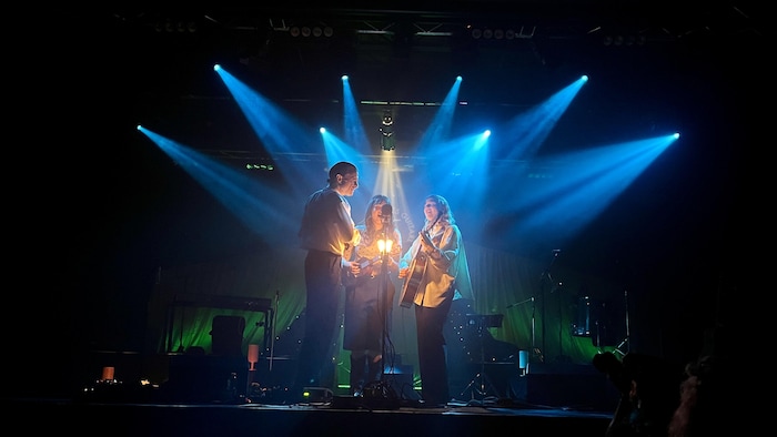 Elliot Maginot, Mélanie et Stéphanie Boulay chantent autour d'un même micro en jouant des intstruments.