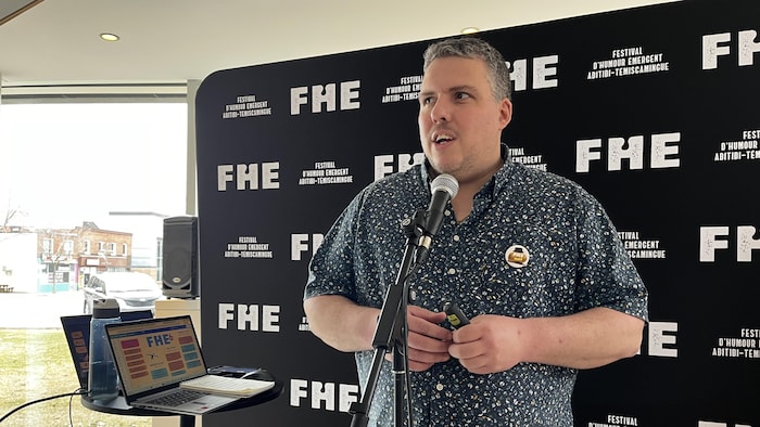 Patrick Gilbert parle au micro devant une affiche du FHE.