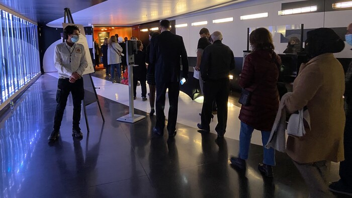 Des personnes attendent devant la porte ouverte d’une salle.
