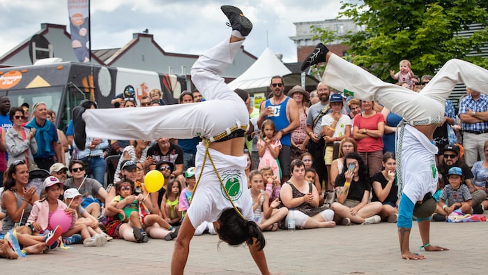 Des artistes se tiennent sur les mains devant une foule réunie sur la rue de la Reine, à Gaspé.