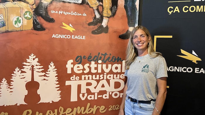 Karine Roberge, présidente du Festival de musique trad de Val-d'Or, pose devant l'affiche du Festival de musique trad de Val-d'Or.