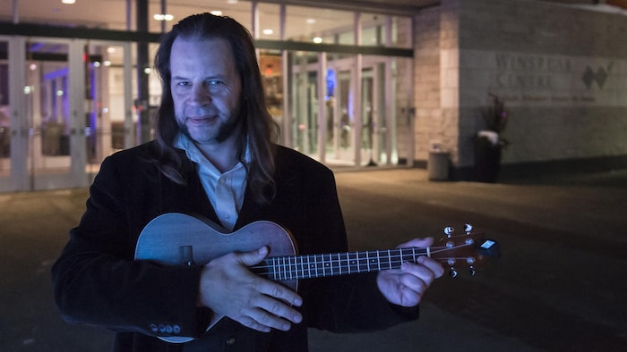 Portrait de Steve Pirot tenant un ukulele devant le centre Winspear d'Edmonton.