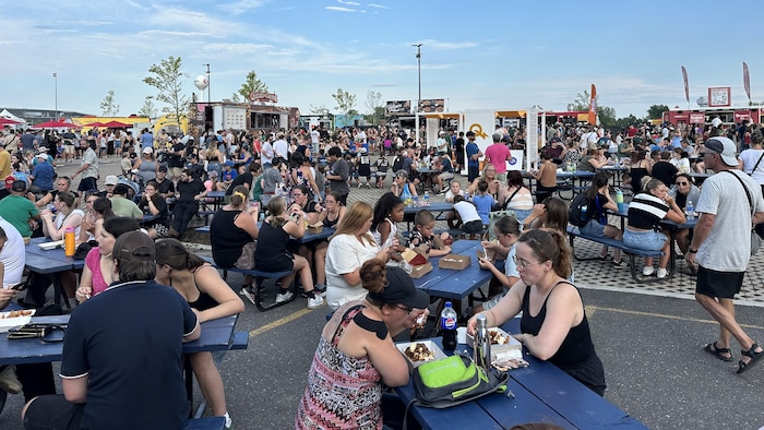 Des centaines de personnes attablées à des tables à pique-nique.