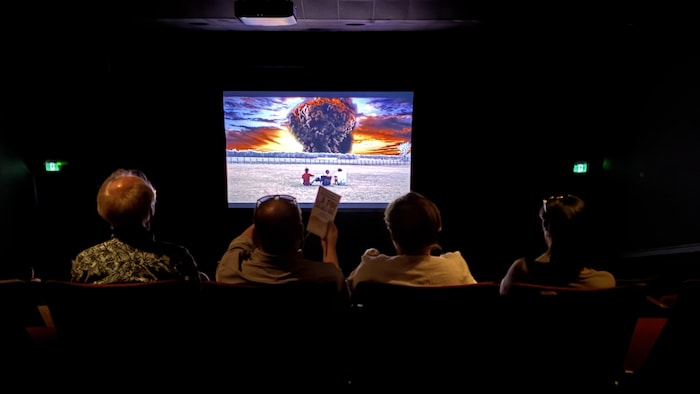 Quatre personnes vues de dos, assises dans un cinéma et regardant l'une des productions 2026 des élèves qui affiche une grosse explosion à l'écran.