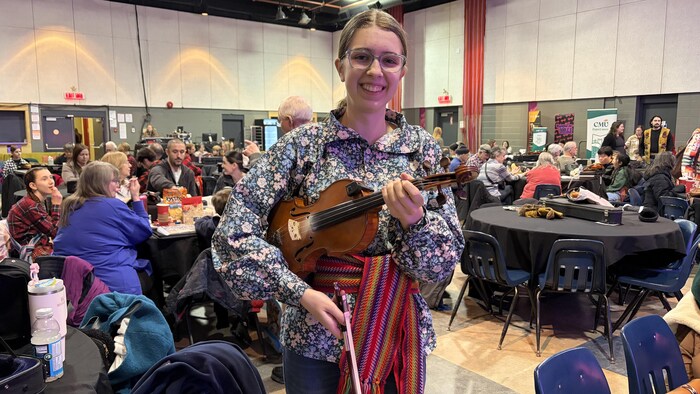 Danika Hutlet souriant avec son violon et sa ceinture fléchée autour de la taille.