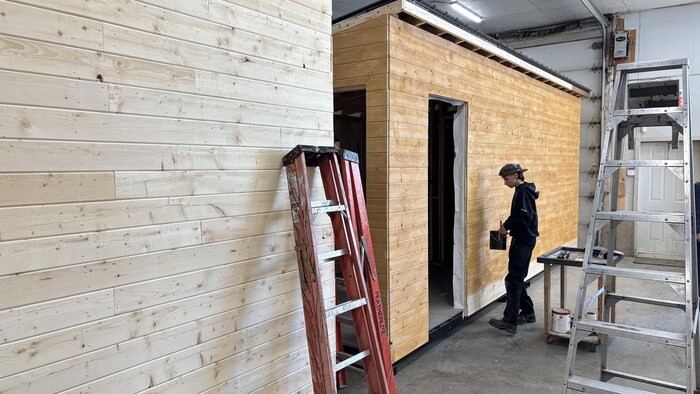 Un jeune homme peint une cabane en bois dans un atelier.