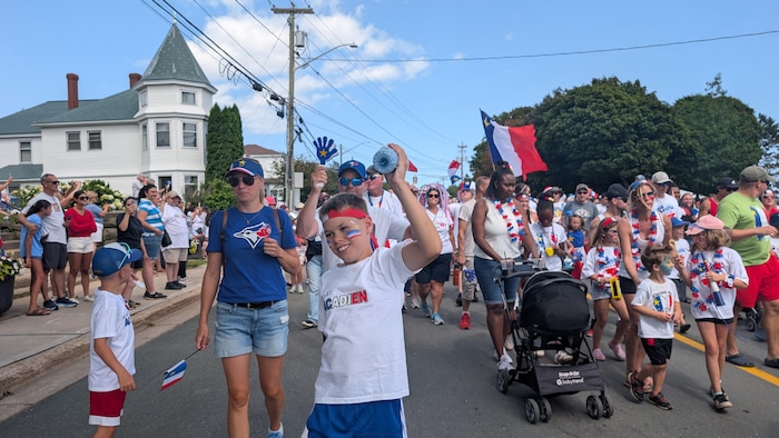 Une foule avec des drapeaux acadiens marche dans la rue.