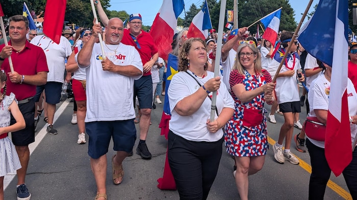 En robe aux couleurs de l'Acadie, Susan Holt avance dans une foule et agite un drapeau.