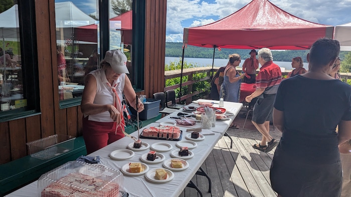 A person places a piece of cake on a small plate and people around speak together.