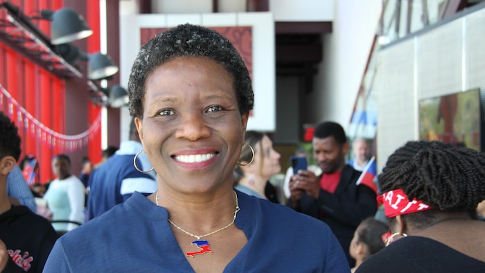 Une femme sourit à l'intérieur du Théâtre Cercle Molière à Winnipeg. Derrière elle, plusieurs personnes ont des drapeaux d'Haïti.