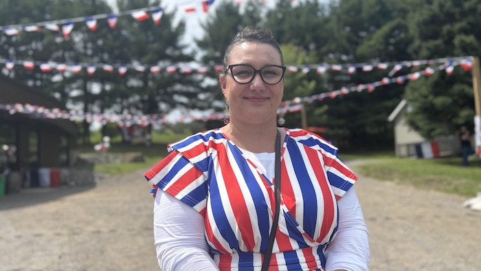 Une femme portant une robe aux couleurs du drapeau français sourit à la caméra, dehors.