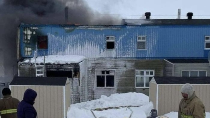 Des pompiers regardent une épaisse fumée s'échapper d'un bâtiment.