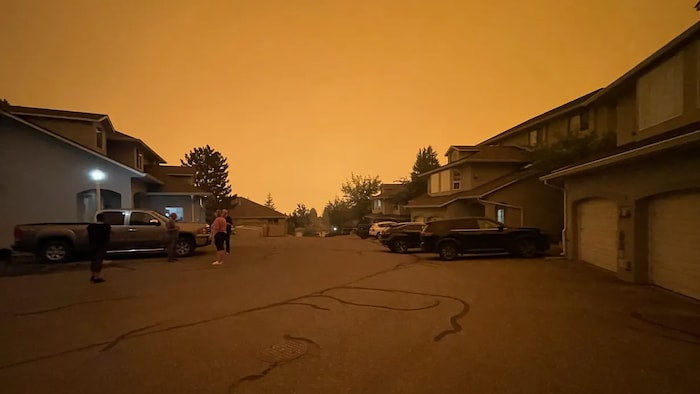 Des personnes discutent dans un lotissement, sous un ciel jaune à cause de la fumée.