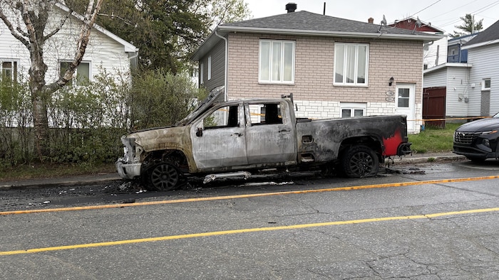 Une camionnette de type « pick up » est brûlée. Elle est stationnée dans la rue, où un périmètre de sécurité a été érigé.